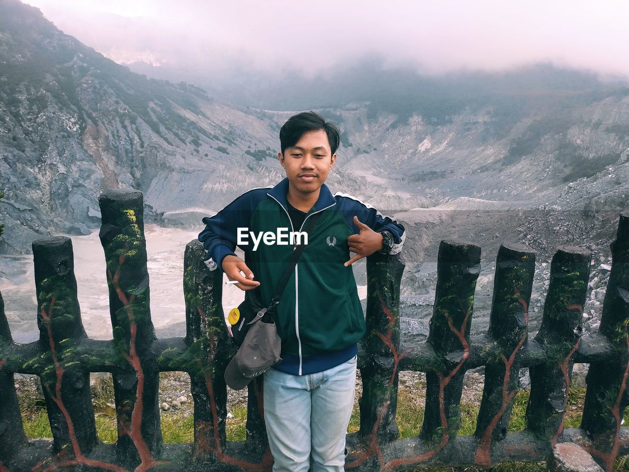 PORTRAIT OF YOUNG MAN STANDING ON MOUNTAINS AGAINST SKY