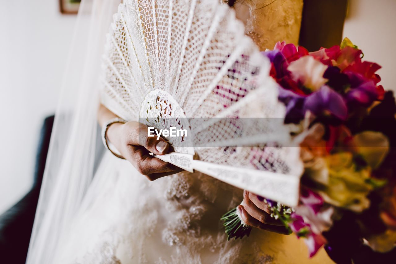 Midsection of bride holding fan and flower bouquet