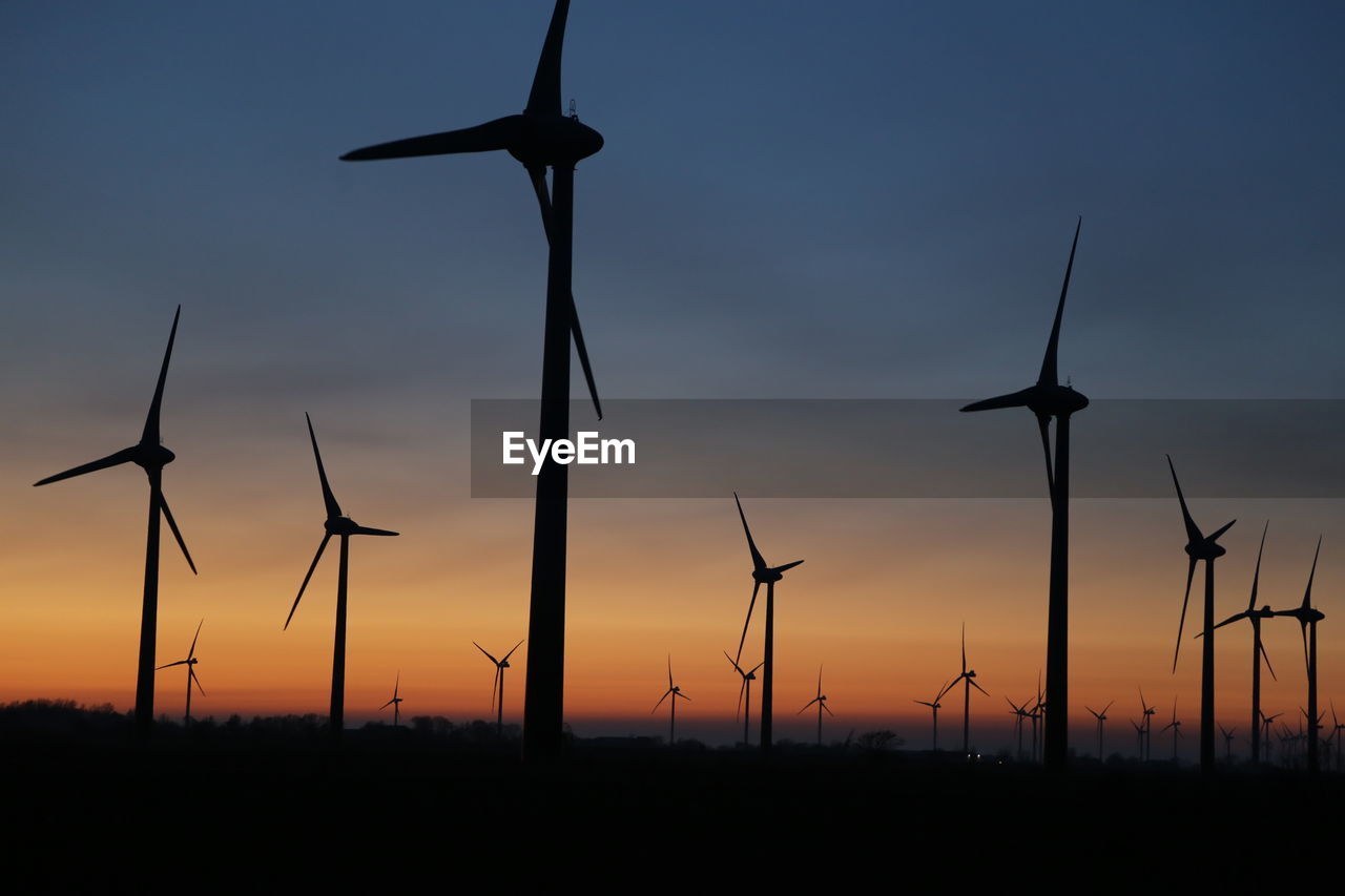 Silhouette wind turbines on field against sky during sunset