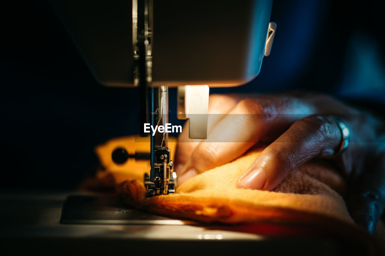 Cropped hand of woman using sewing machine in dark workshop