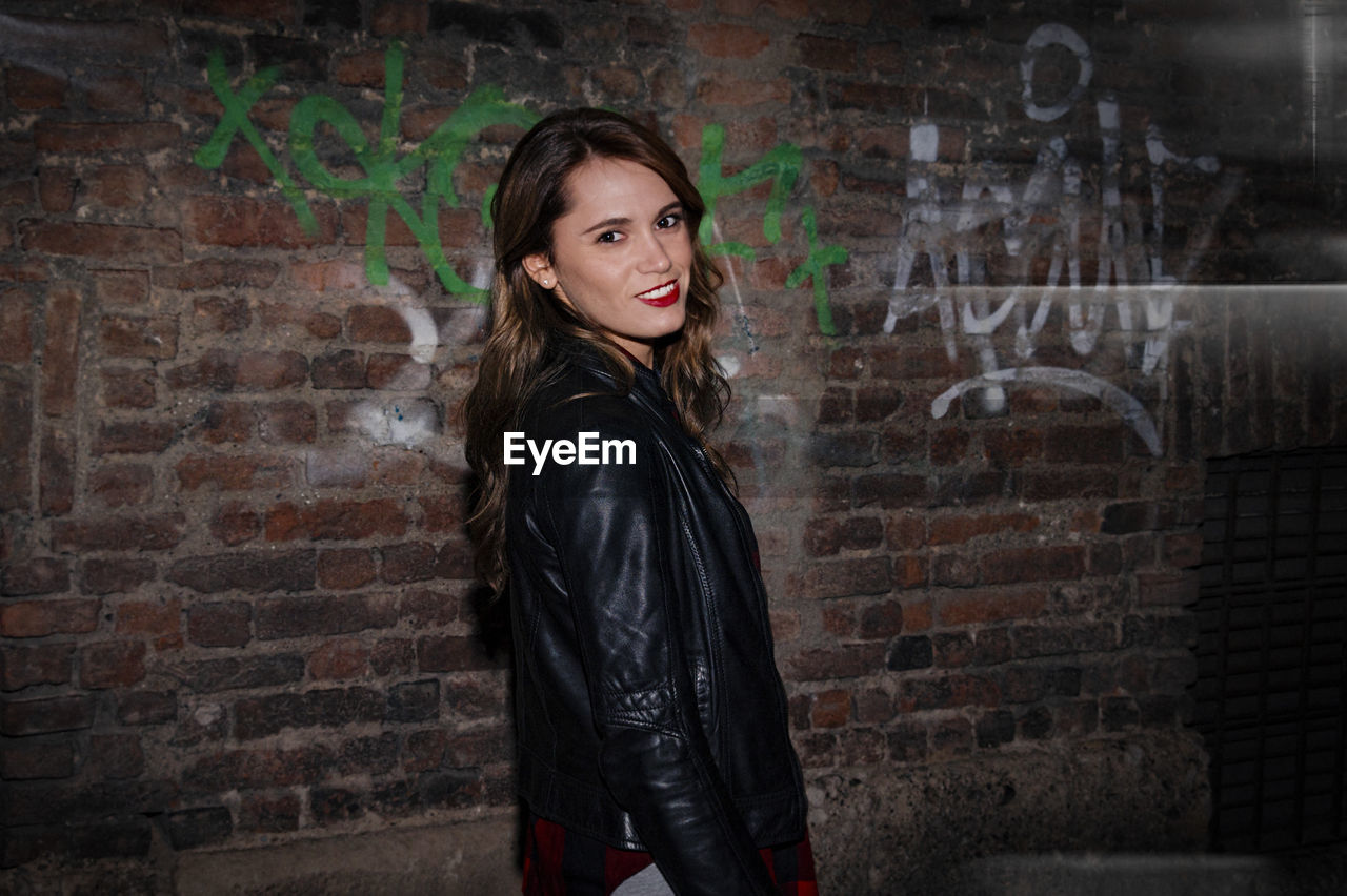 Portrait of beautiful woman standing by old graffiti wall