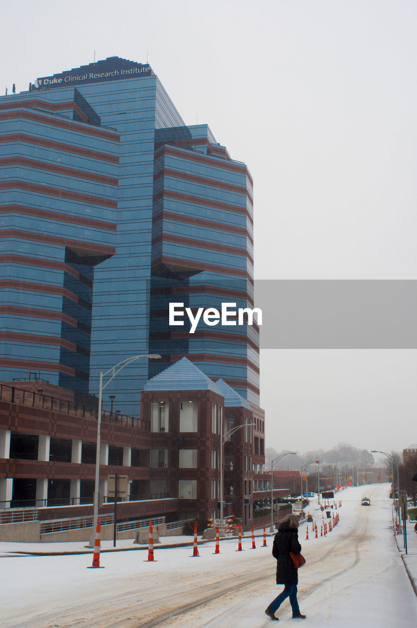 Woman crossing road against modern building in winter