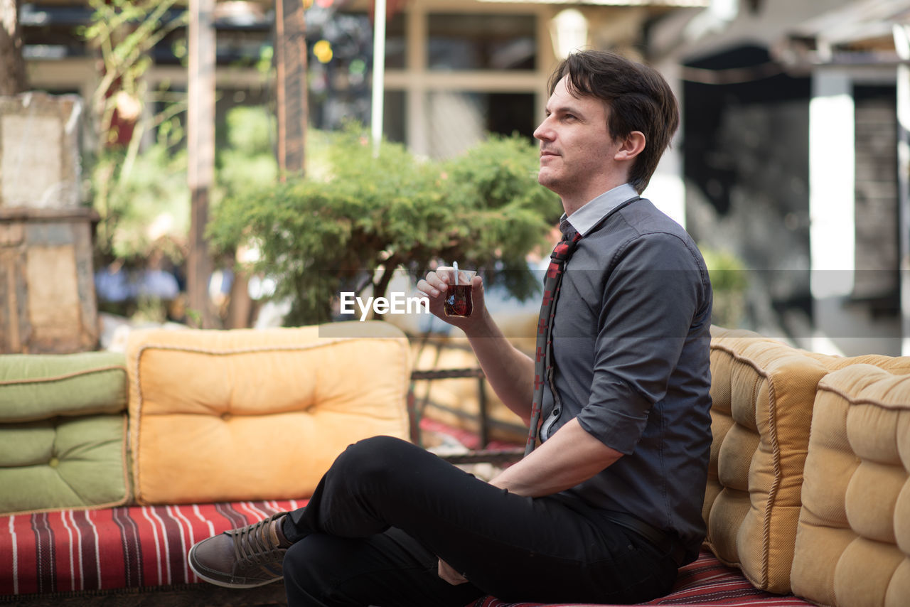 Young man holding drink sitting on sofa