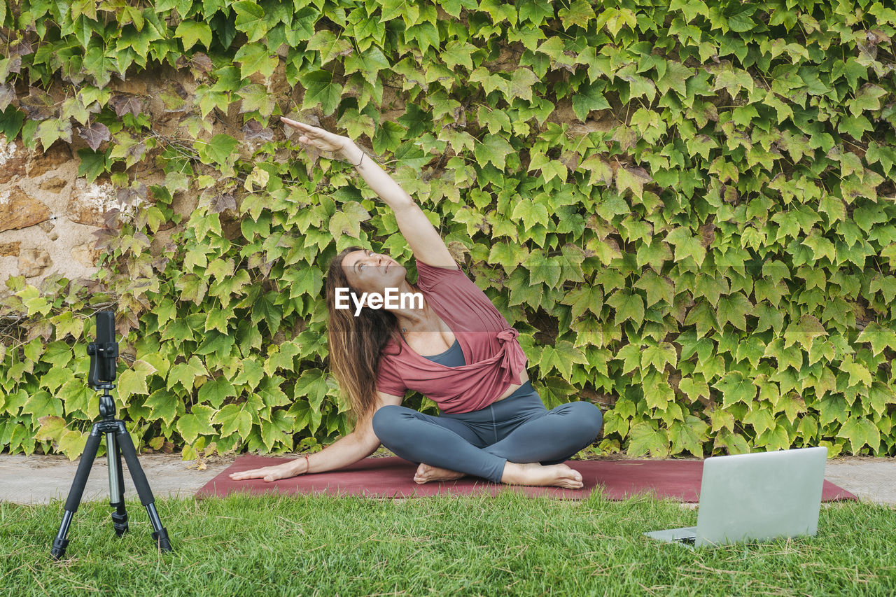 Woman teaching yoga during online yoga class with mobile phone and laptop