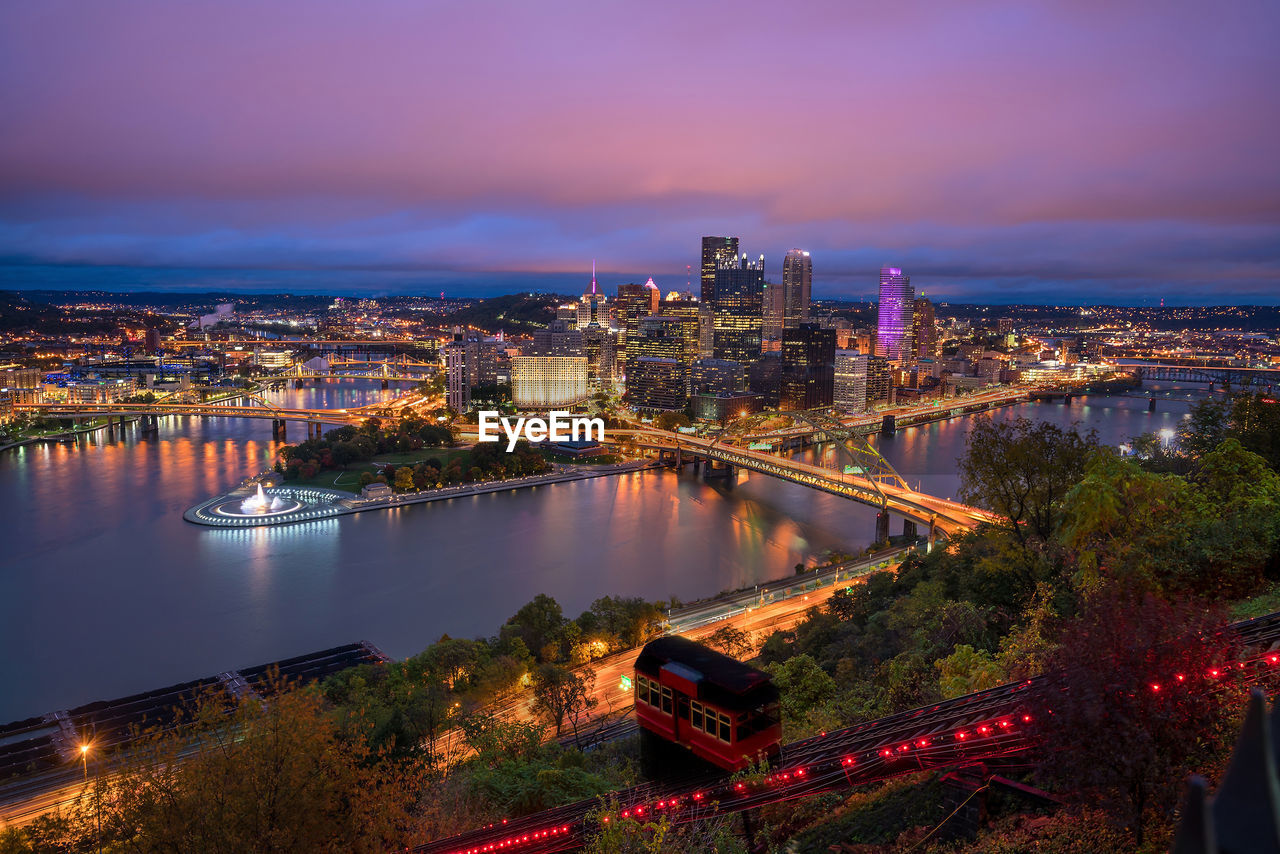 high angle view of illuminated buildings by river against sky at night