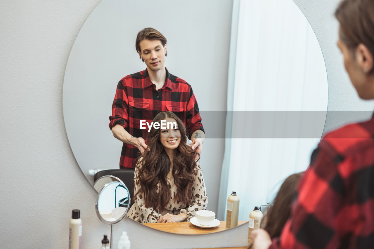 Stylist barber styling long hair for beautiful asian young woman in the beauty salon, working moment