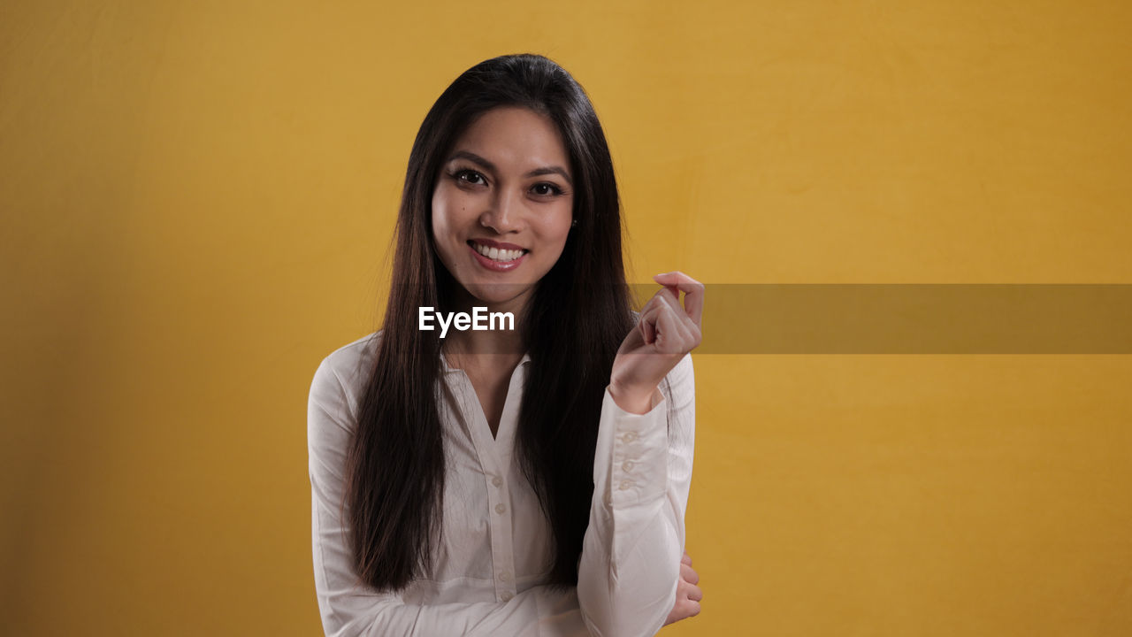 portrait of beautiful young woman standing against yellow background