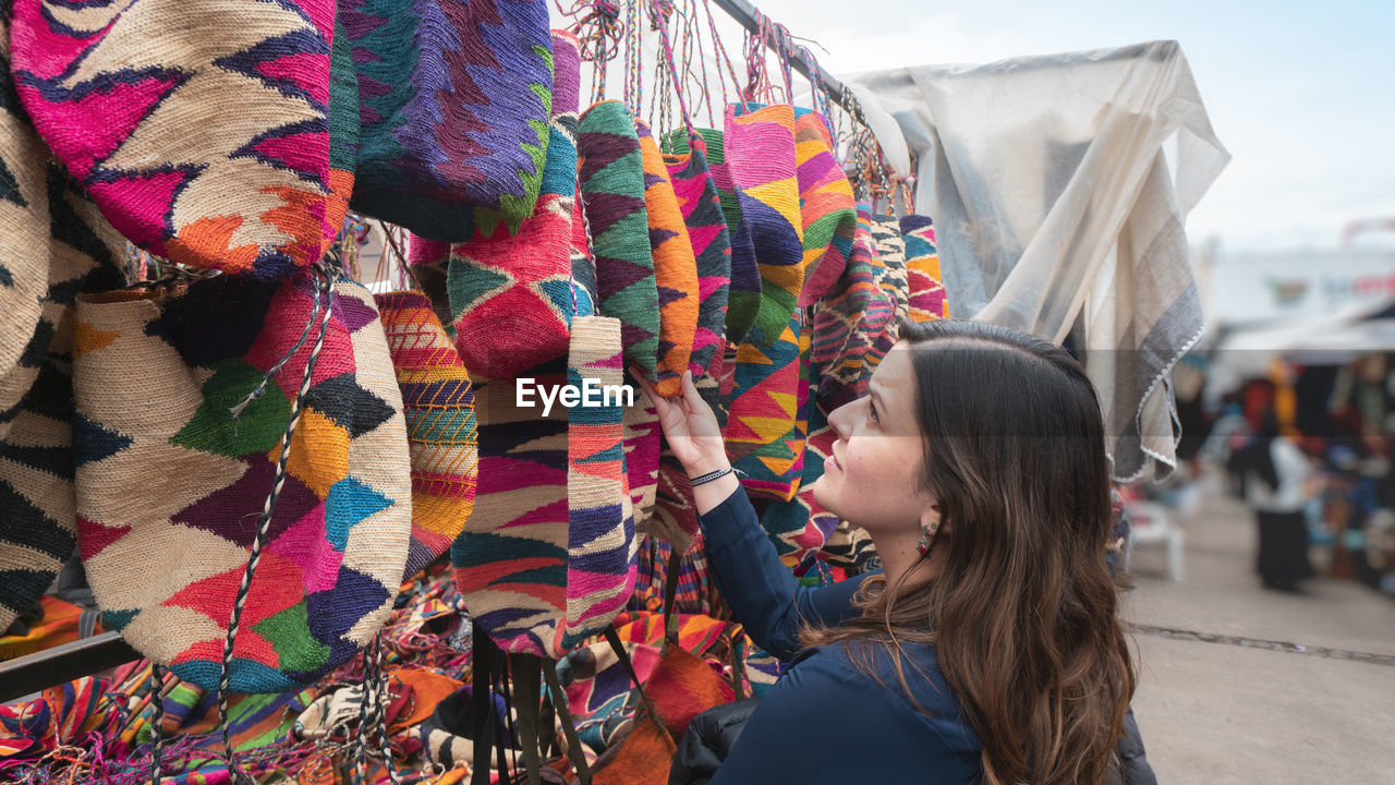 Young latin american woman comparing shigras that hang for sale in the plaza de los ponchos