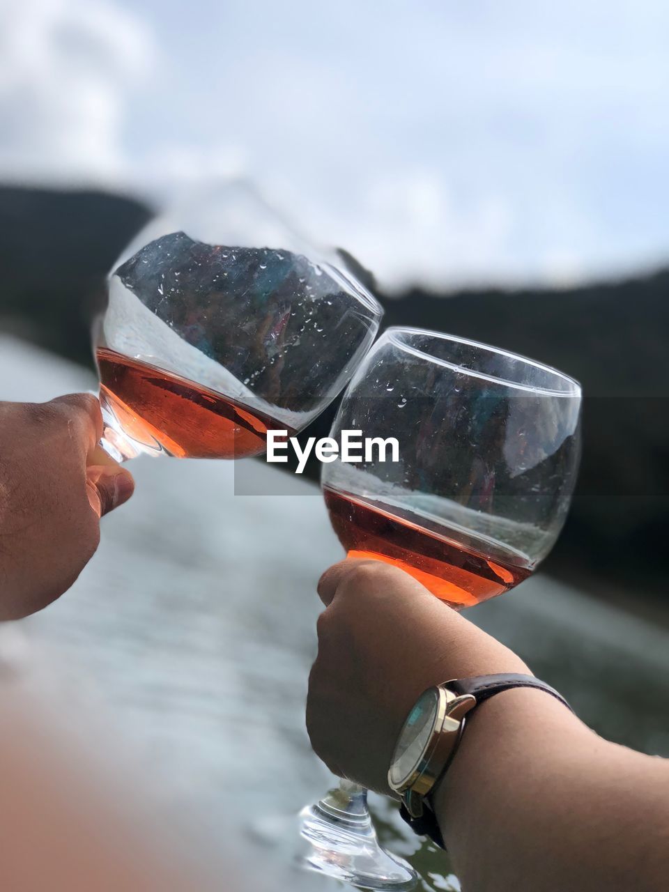 Cropped hands of friends toasting wineglasses against lake