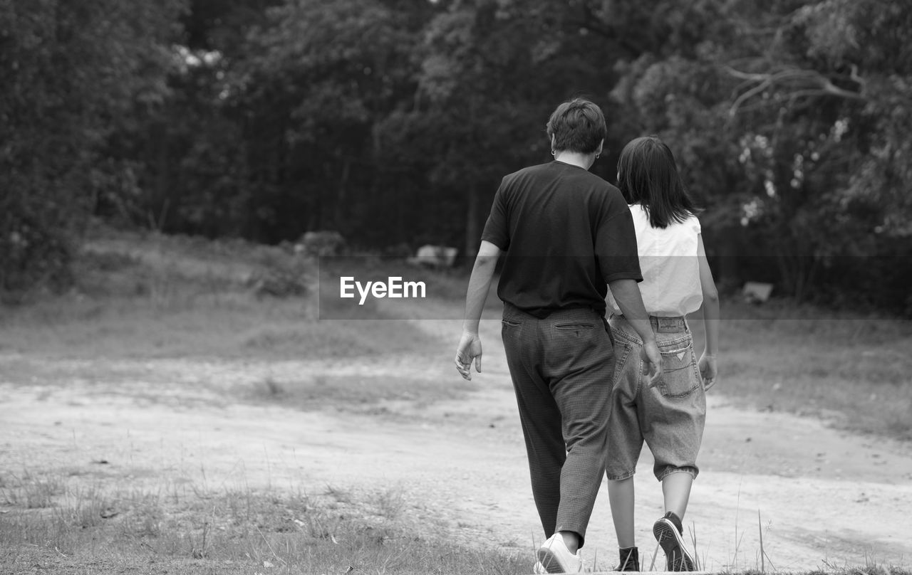 REAR VIEW OF COUPLE WALKING ON STREET AMIDST TREES