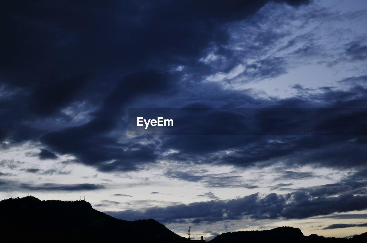 LOW ANGLE VIEW OF STORM CLOUDS OVER SILHOUETTE MOUNTAINS