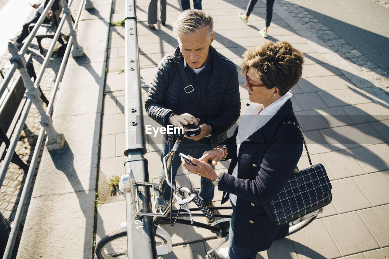 High angle view of senior couple using mobile phones while standing on sidewalk in city