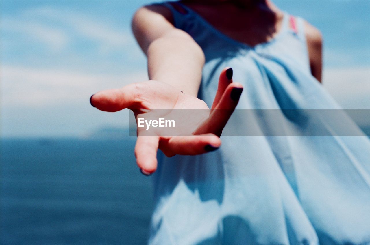 Midsection of woman gesturing while standing against sea