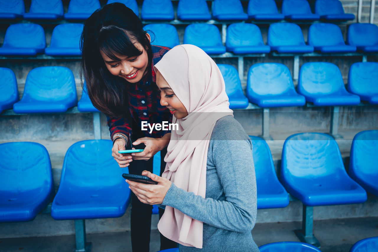 FULL LENGTH OF SMILING YOUNG WOMAN USING MOBILE PHONE IN LAPTOP