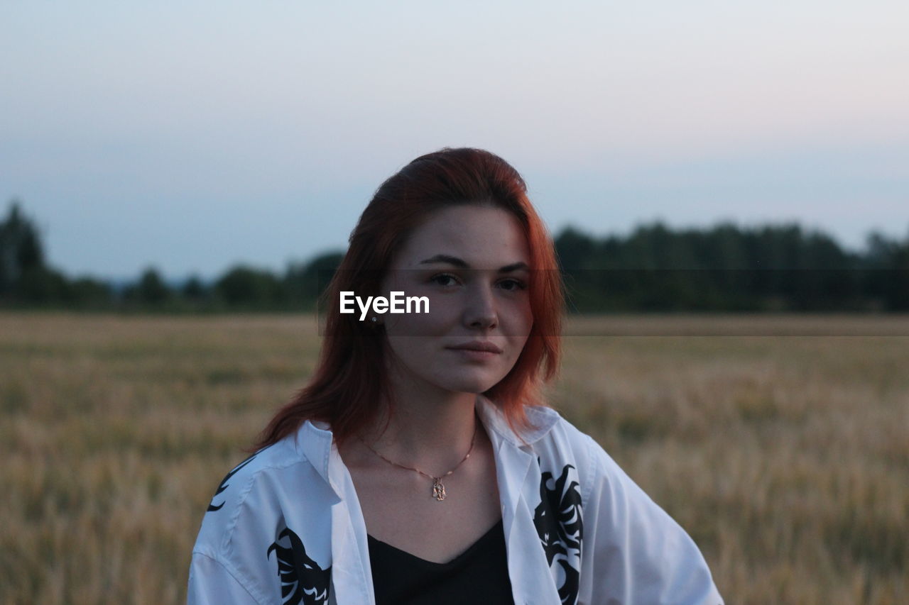 Portrait of young woman standing on field against sky