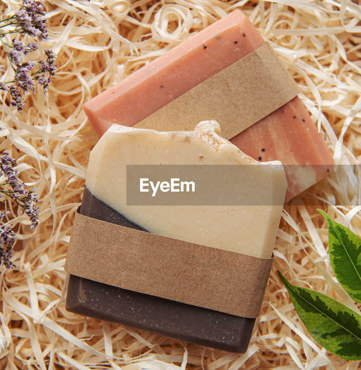 Assorted natural handmade soap bars and green leaves on a straw background