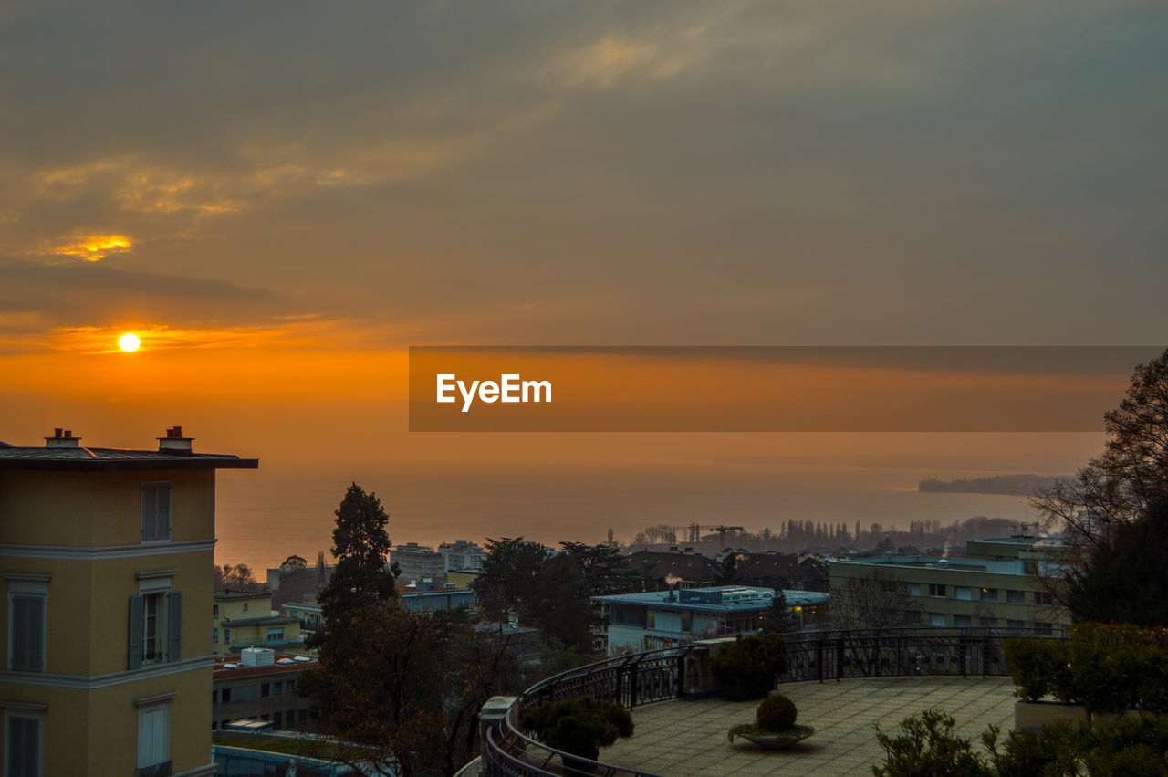 HIGH ANGLE VIEW OF BUILDINGS AND TREES AGAINST SKY AT SUNSET