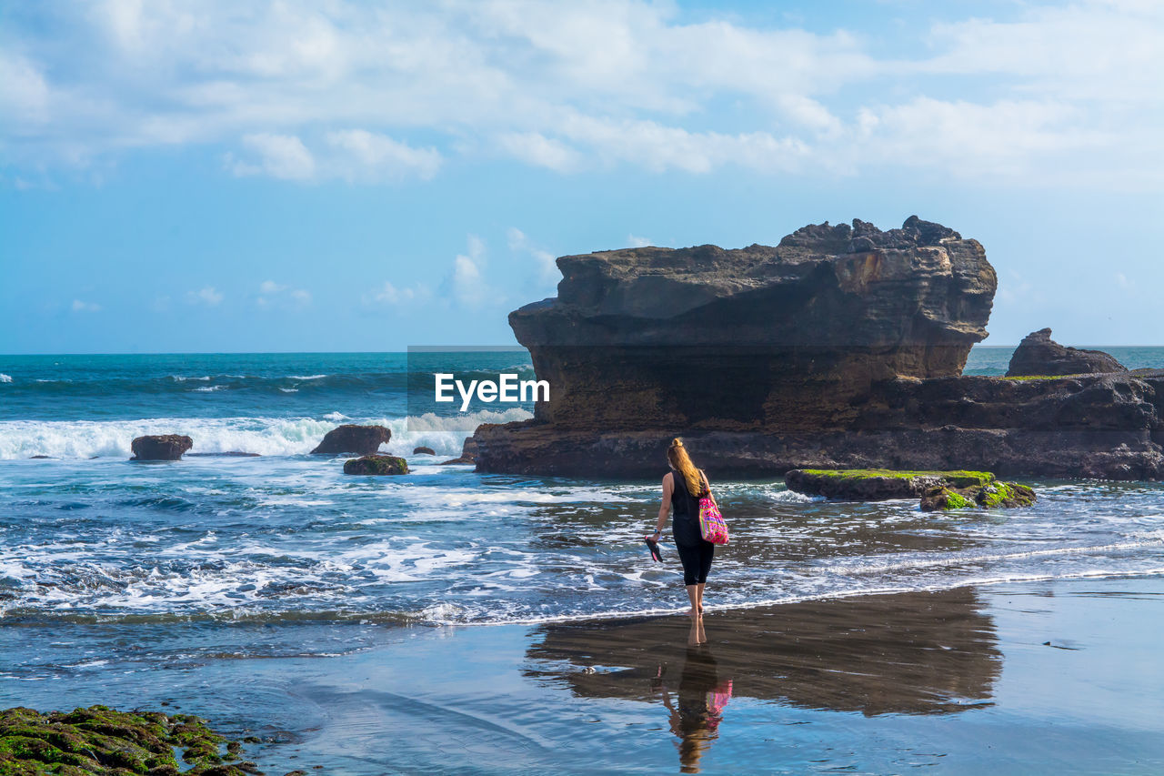 Rear view of woman walking on shore at beach against sky