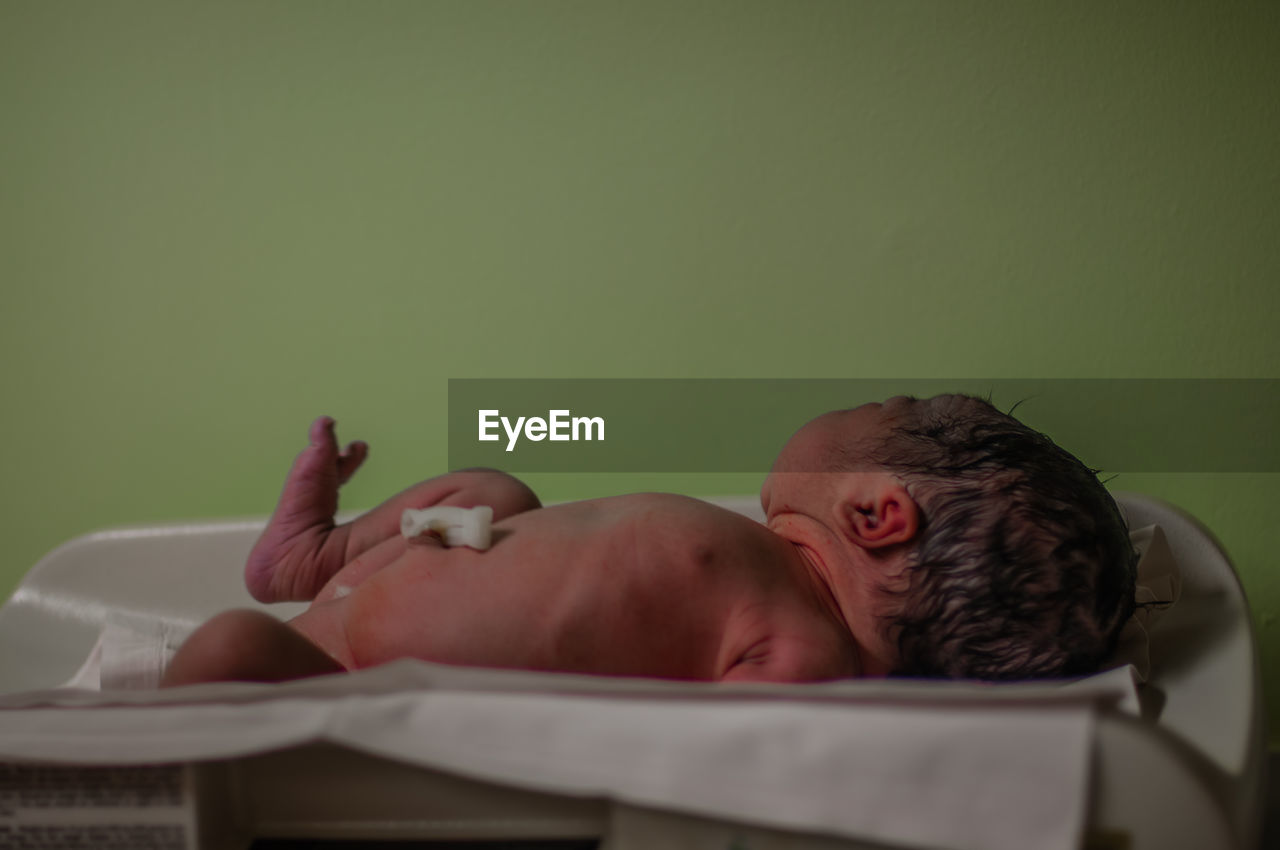 Newborn baby lying in crib against green wall