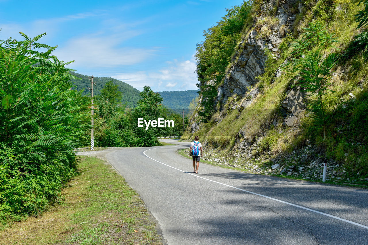 Rear view of man walking on road by mountain