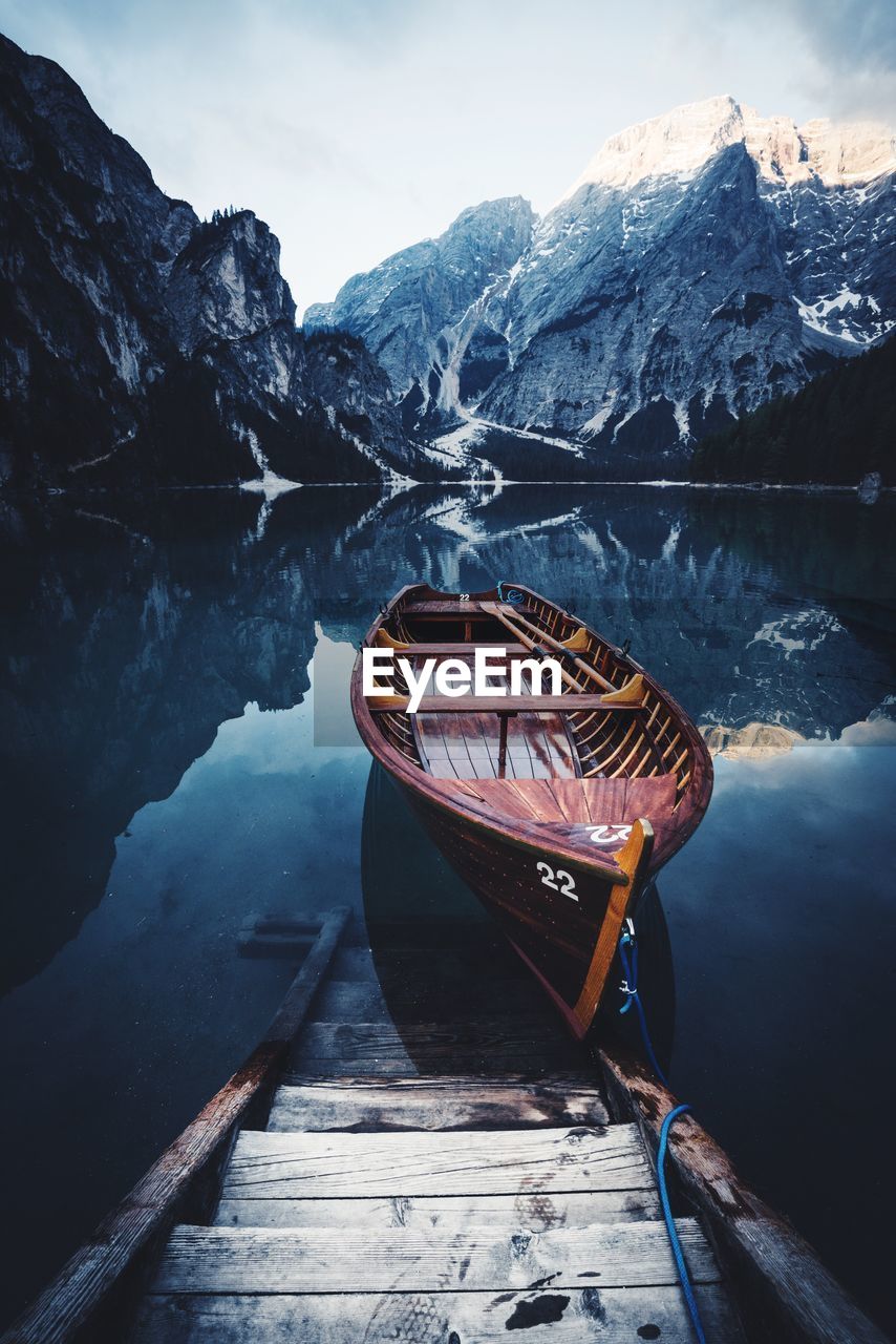 Boat moored on calm lake against mountain during winter