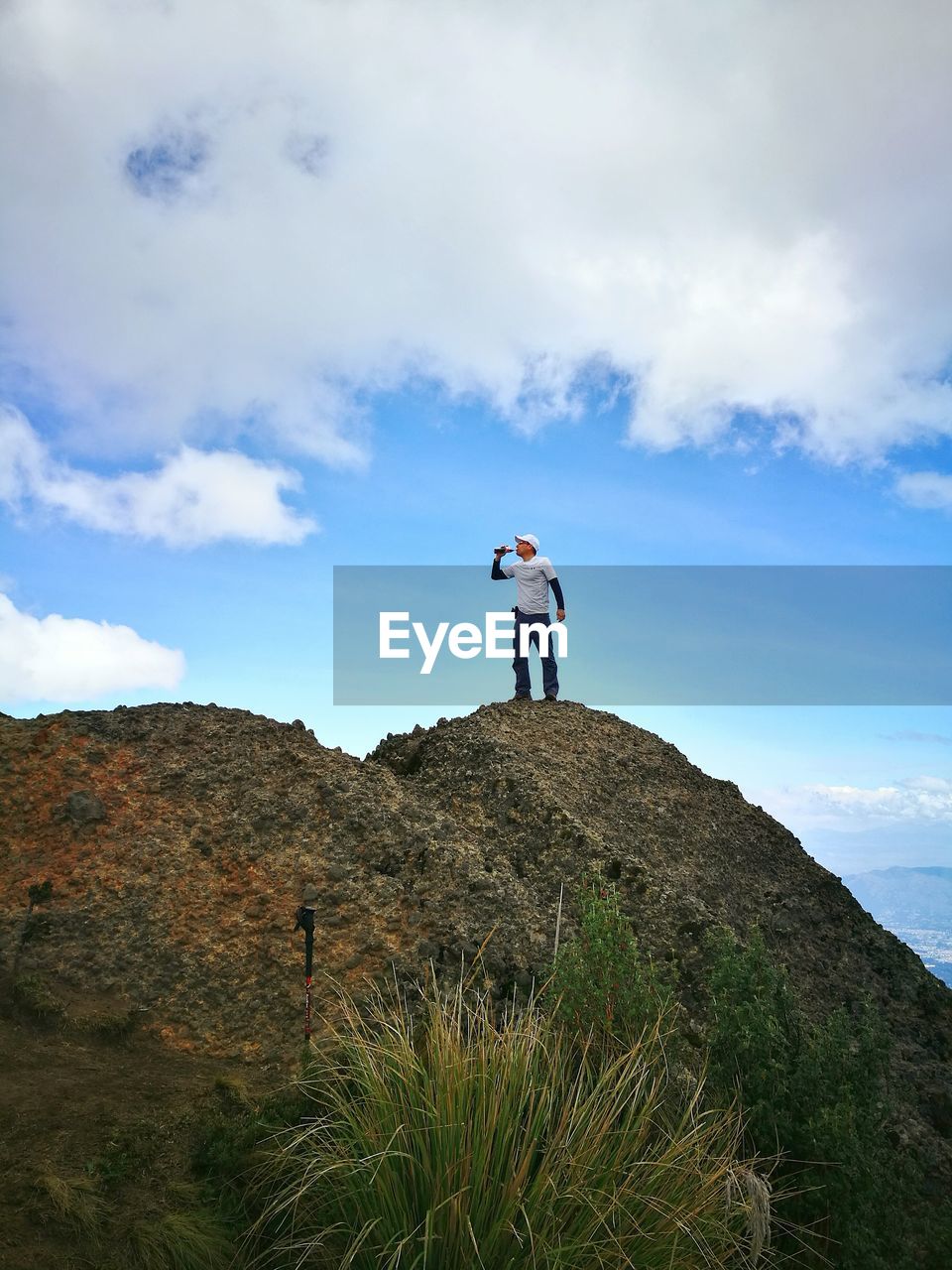 Low angle view of man drinking while standing on mountain against cloudy sky