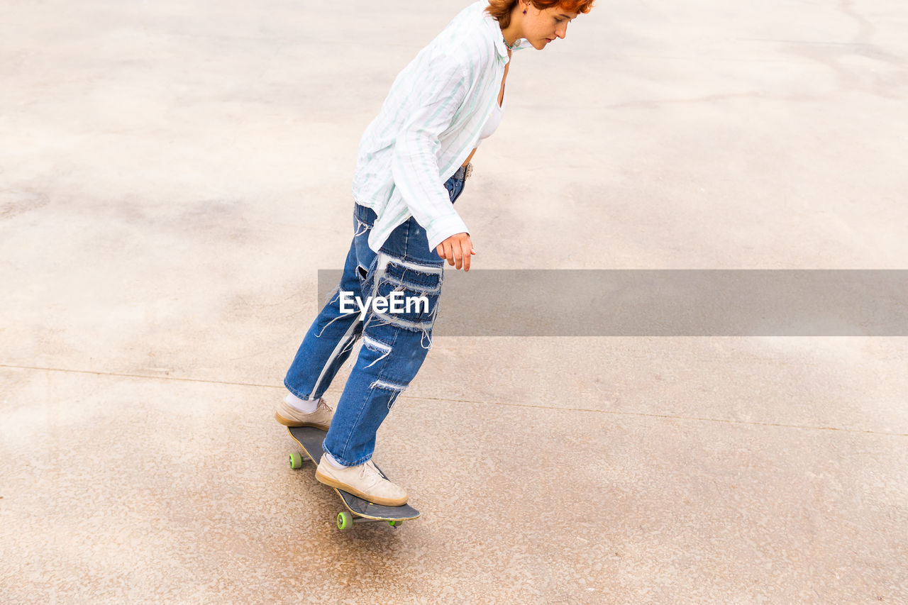 From above side view of active female in casual wear riding skateboard in skate park with ramp on summer day