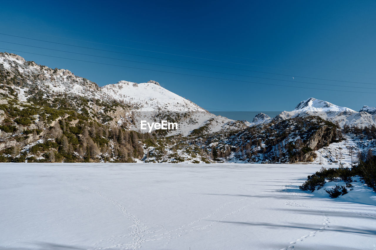 snow, winter, cold temperature, mountain, scenics - nature, landscape, environment, sky, beauty in nature, nature, tree, mountain range, plant, snowcapped mountain, blue, coniferous tree, tranquil scene, pine tree, land, tranquility, piste, pinaceae, no people, forest, clear sky, travel destinations, pine woodland, frozen, white, non-urban scene, travel, day, outdoors, winter sports, sunny, mountain peak, sunlight