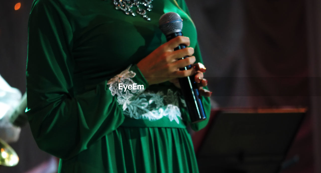 Midsection of woman in traditional clothing holding microphone while standing on stage