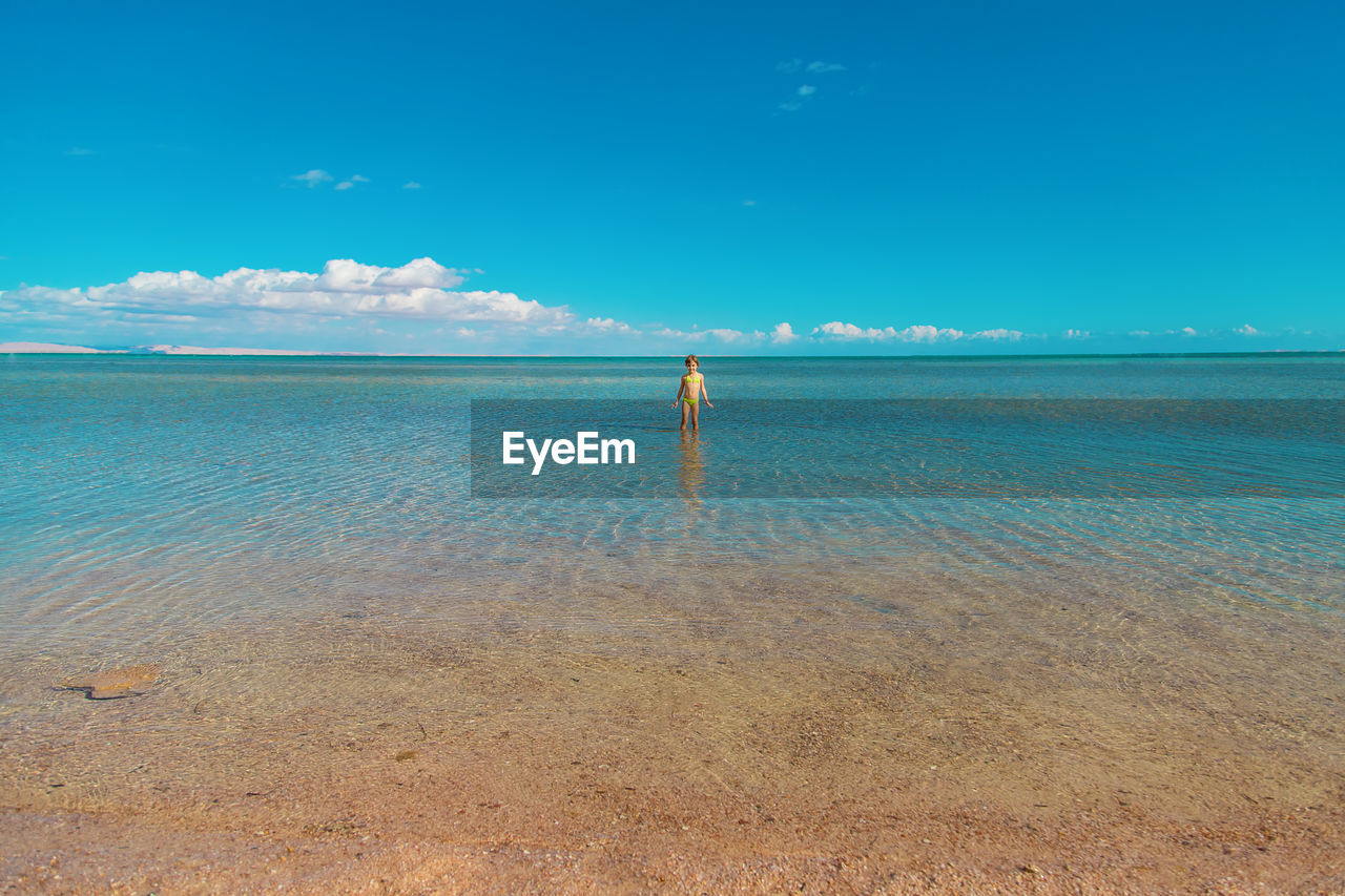 rear view of woman walking at beach against blue sky