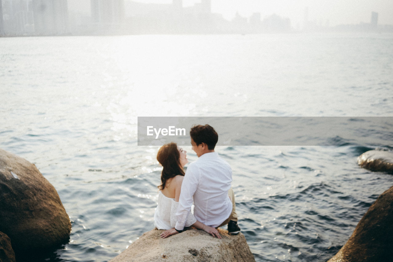 Rear view of couple sitting on rock by sea