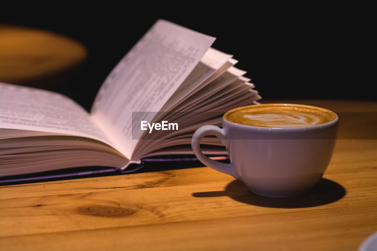 CLOSE-UP OF COFFEE CUP ON TABLE AGAINST BOOK