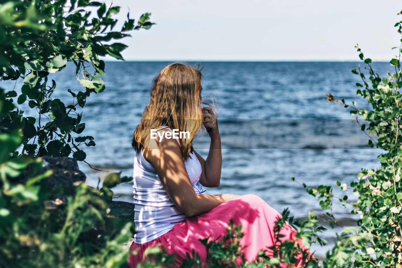 Woman pregnant sitting by sea against sky