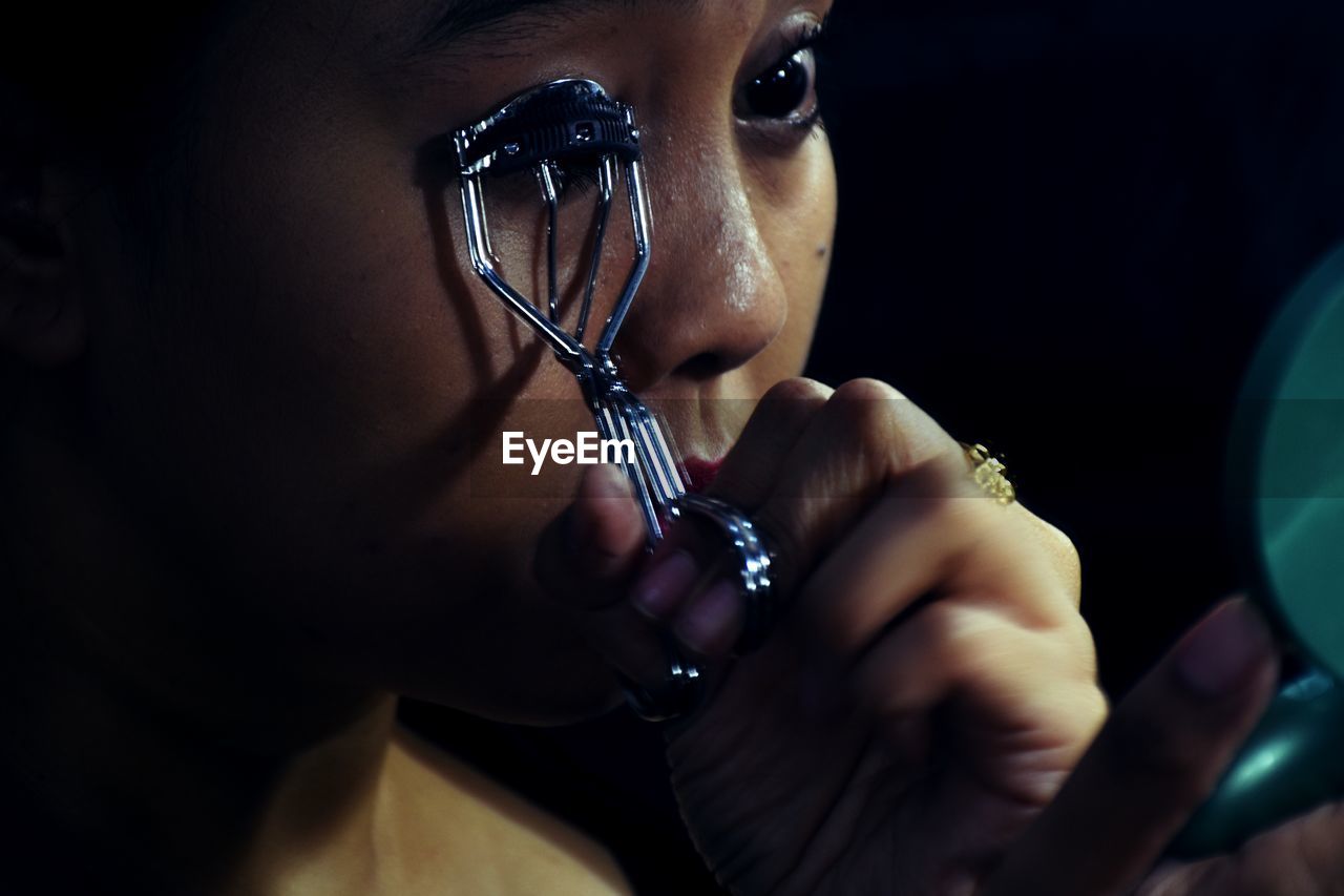 Close-up of woman using eyelash curler while looking at mirror