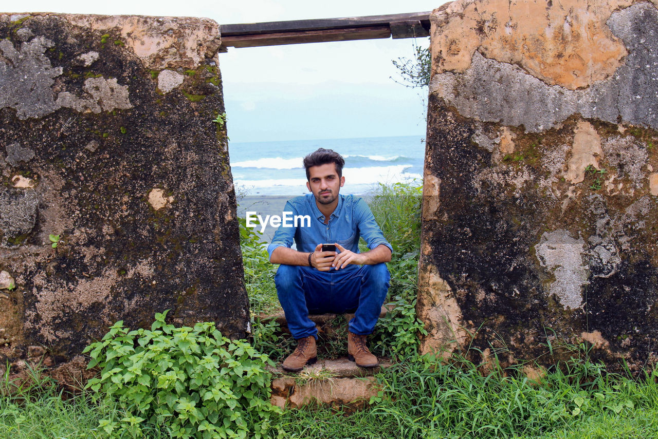 Full length portrait of young man sitting on rock