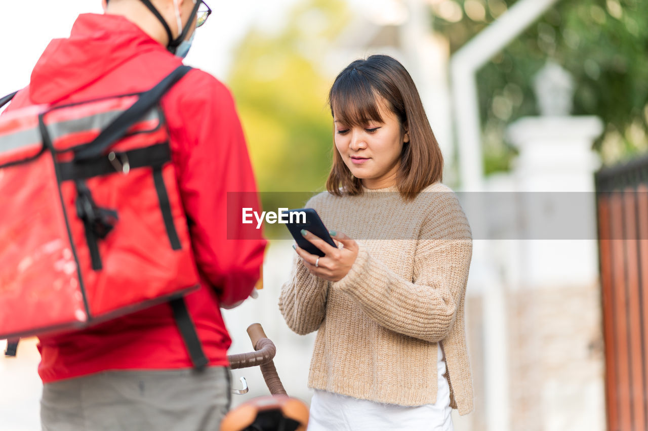 YOUNG WOMAN USING SMART PHONE WHILE STANDING ON MOBILE