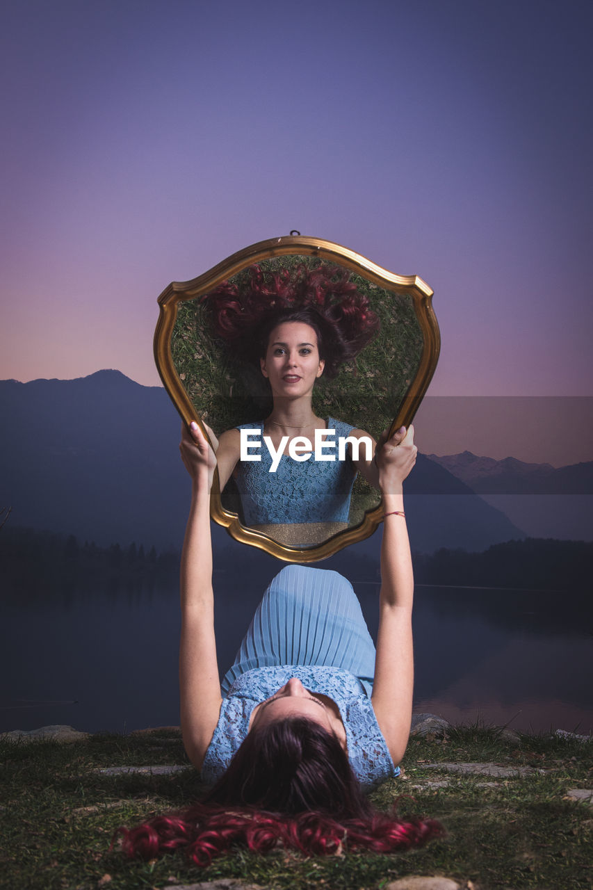 Woman holding mirror with her reflection against mountains