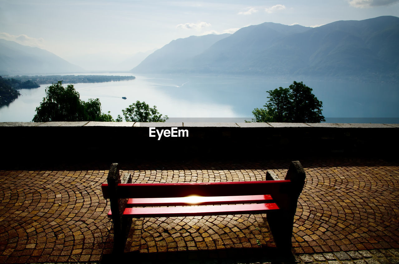 Empty bench by lake against sky