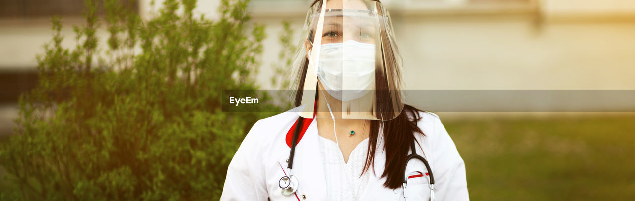 Woman wearing face shield standing against plant