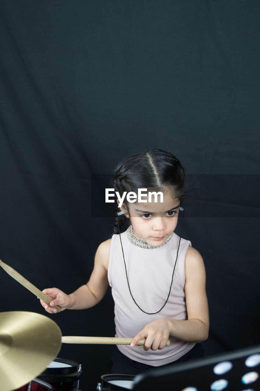 Girl playing drum while standing against curtain