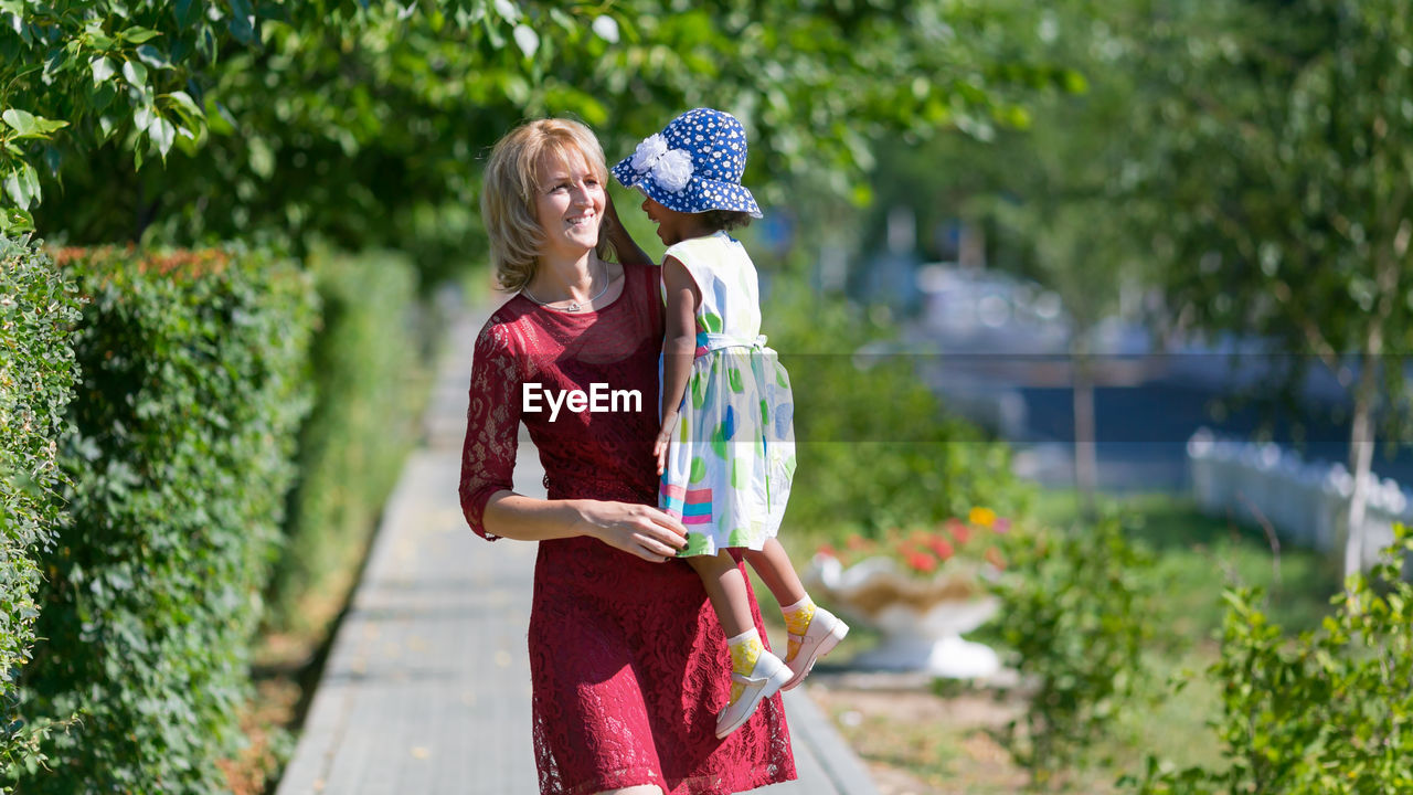 Mother carrying daughter at park on sunny day