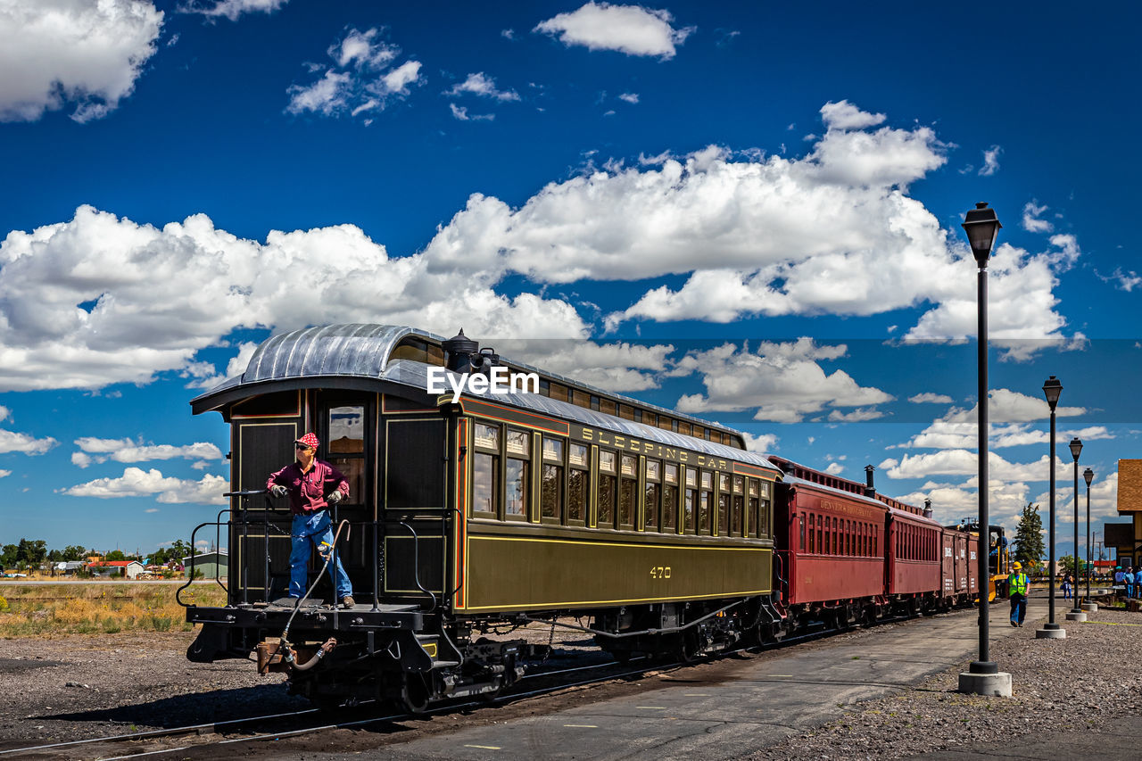 transportation, mode of transportation, sky, cloud, train, rail transportation, transport, vehicle, railway, railroad track, travel, track, land vehicle, public transportation, locomotive, nature, electricity, architecture, rolling stock, travel destinations, station, outdoors, on the move, blue, day, passenger, motion, railroad car, city, metropolitan area, business, journey, tourism, railroad station, business finance and industry