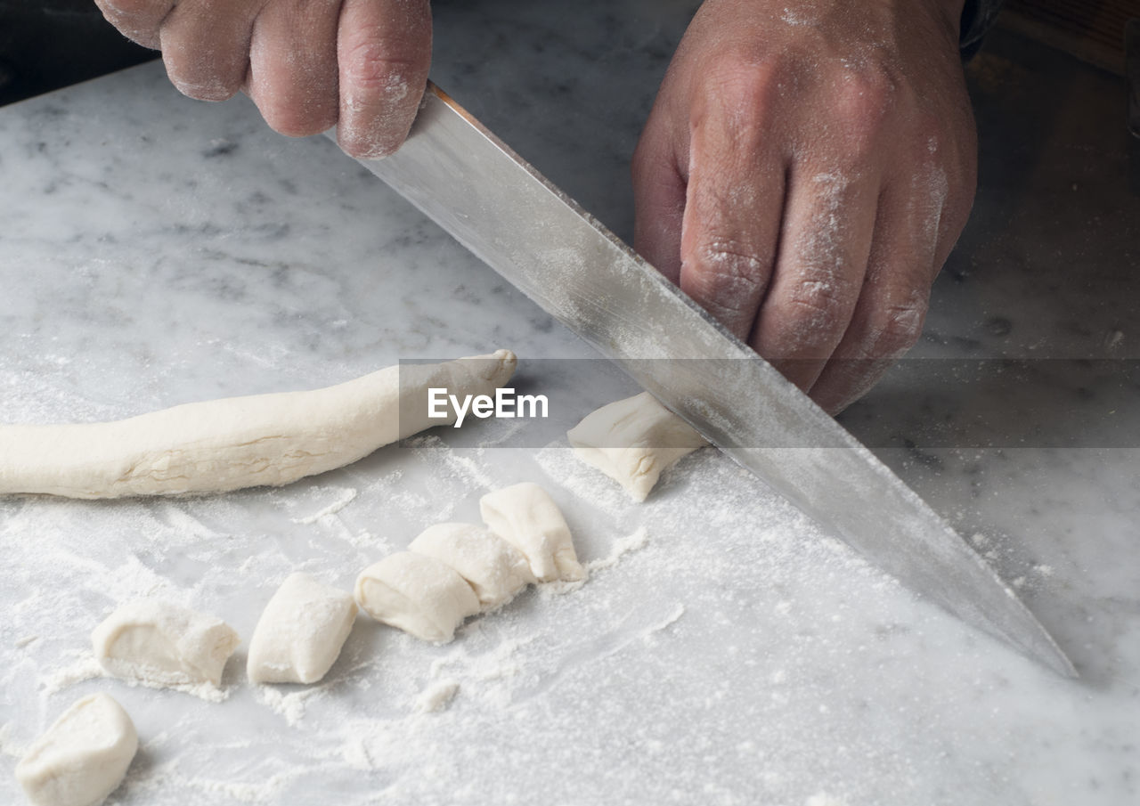 Cropped hands of chef cutting dough on table in commercial kitchen