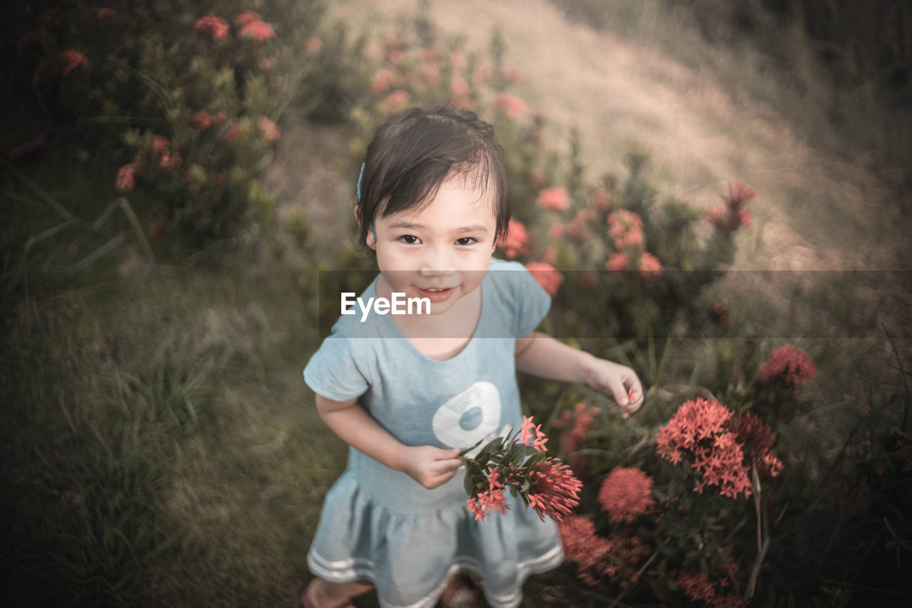 High angle portrait of smiling girl standing by ixora plant on field