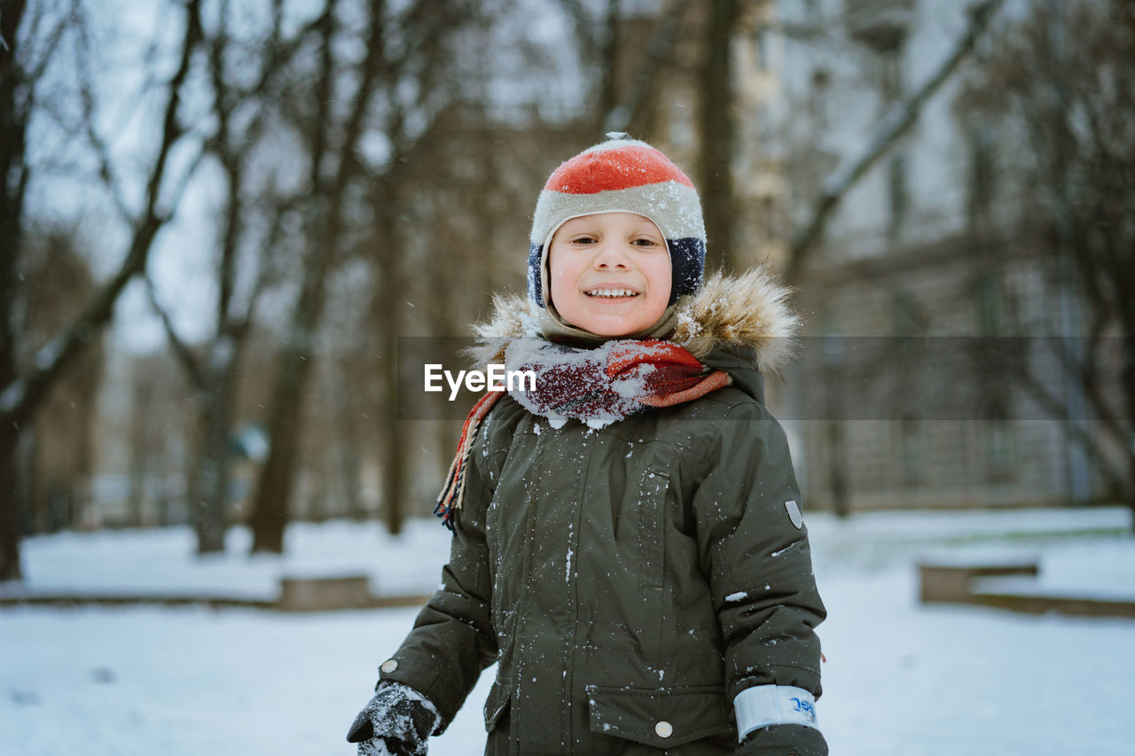 Winter portrait of cute caucasian 7 years old boy in knit hat with pompom in city