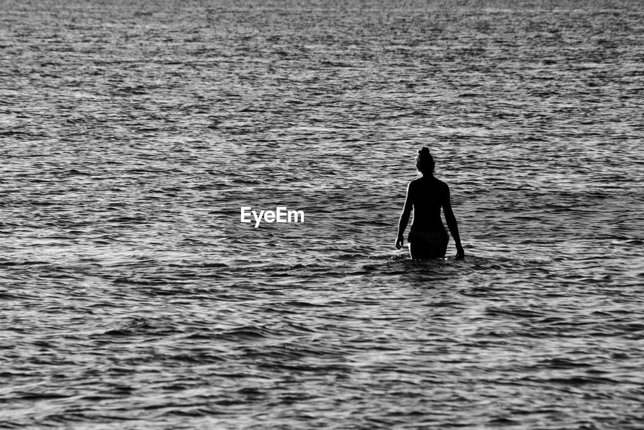 Silhouette of a woman from behind walking in the shallow water at the beach