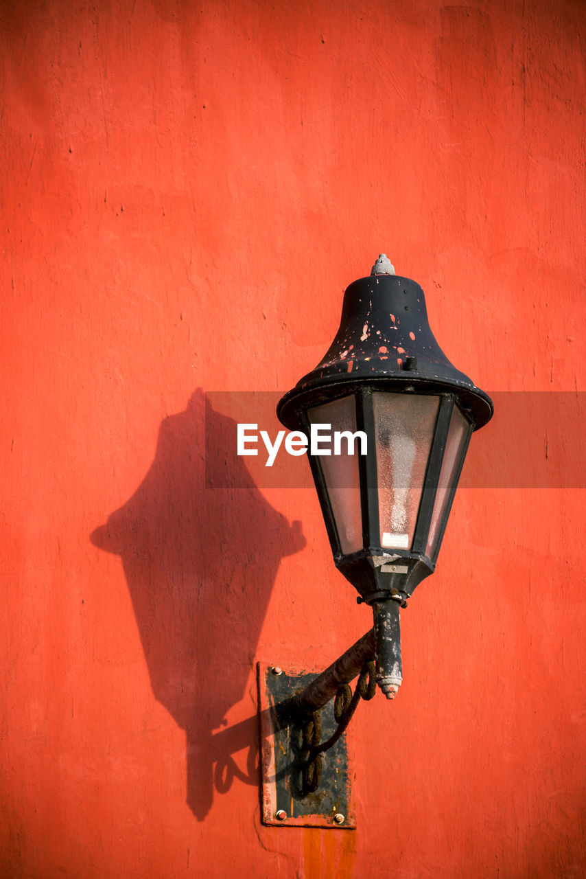 Low angle view of lamp post on red wall during sunny day