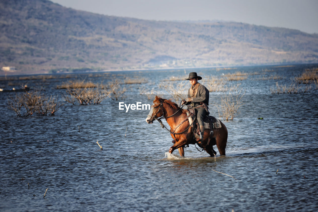 Man riding horse in lake against sky