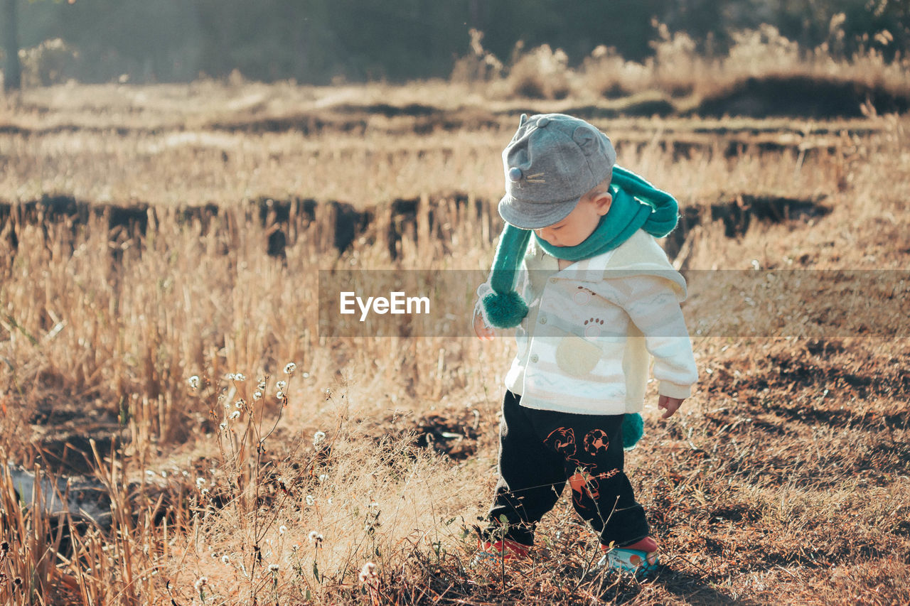 Cute baby boy wearing warm clothing and cap on land