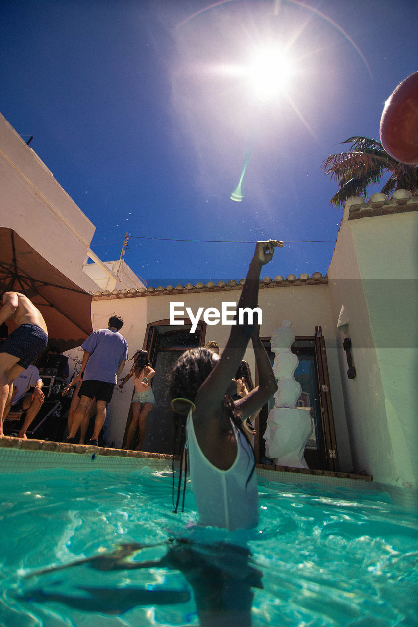 PEOPLE BY SWIMMING POOL AGAINST BLUE SKY